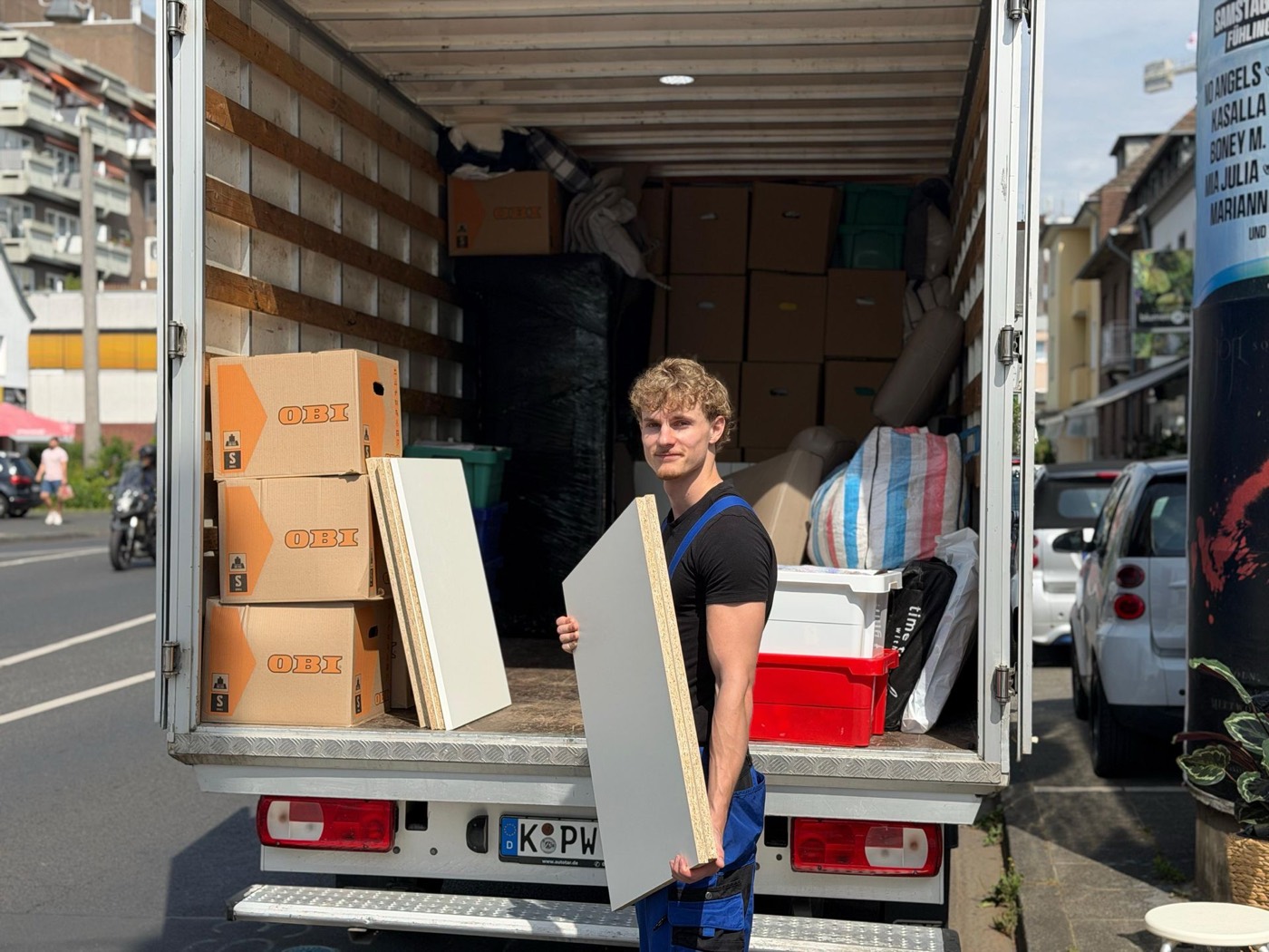 Umzugshelfer mit einer Schranktür vor dem beladenen Wagen