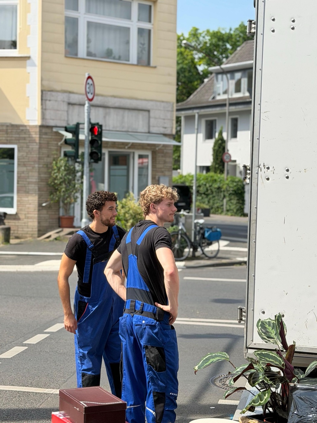 Zwei Umzugshelfer stehen neben dem Wagen vor einem Wohnhaus